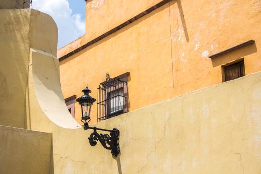 Rustic streetlamp against warm yellow walls in Santiago de Querétaro, Mexico.