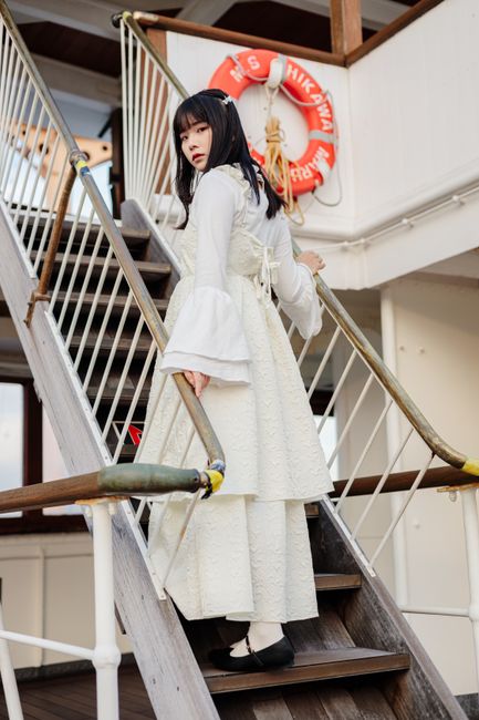 An Asian woman in a white dress stands on a ship's staircase in Yokohama, Japan.