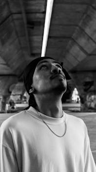 Black and white portrait of a man looking up under a city bridge.