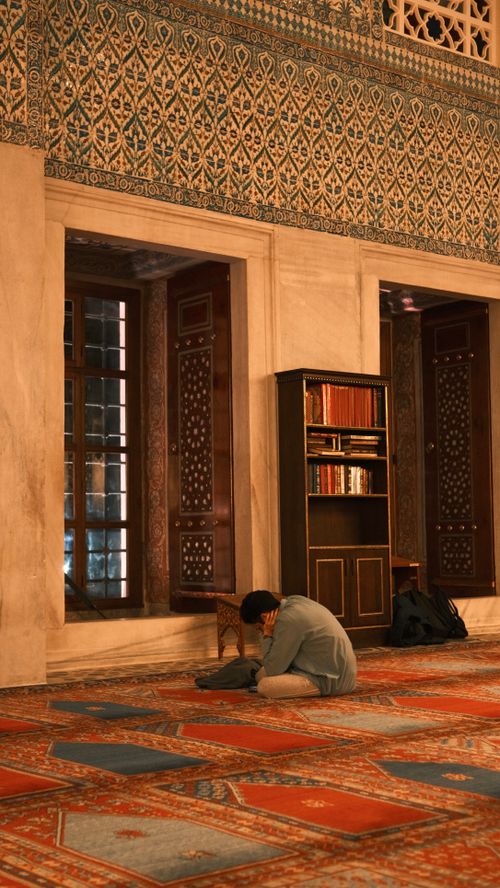 Free A person in meditation inside a beautifully decorated mosque, surrounded by intricate patterns and holy books. Stock Photo