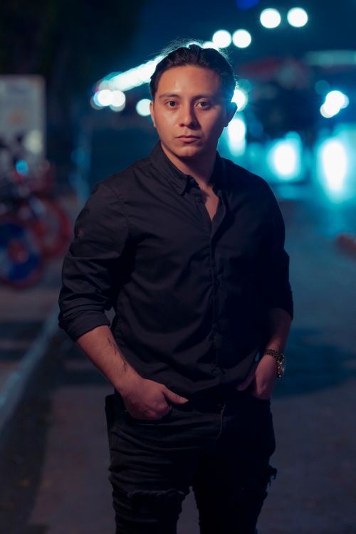 Free Portrait of a confident young man wearing a black shirt standing in a brightly lit urban street at night. Stock Photo