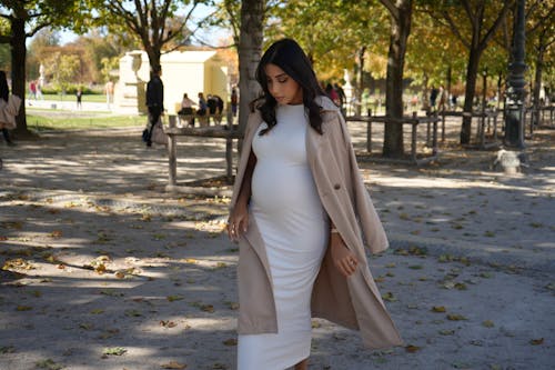 A pregnant woman in a white coat and white dress