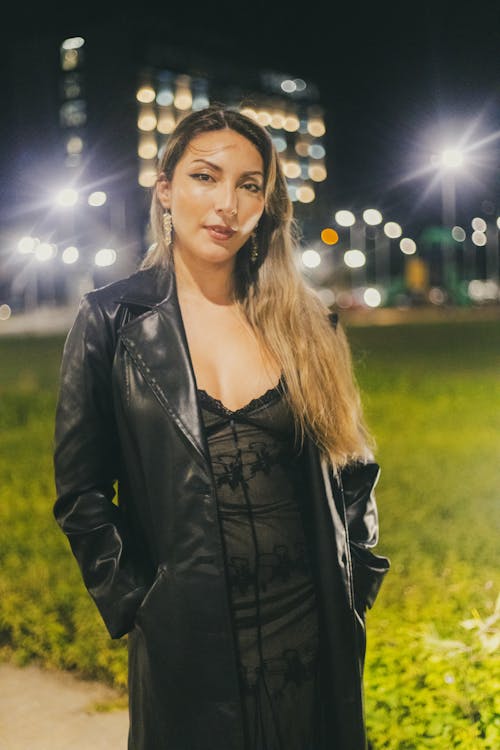 A woman in a black dress and leather jacket at night