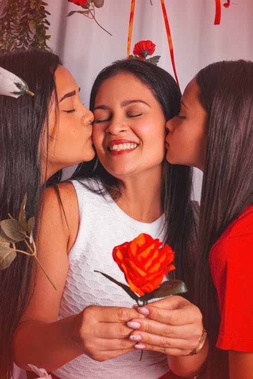 Three women are kissing each other and holding a rose