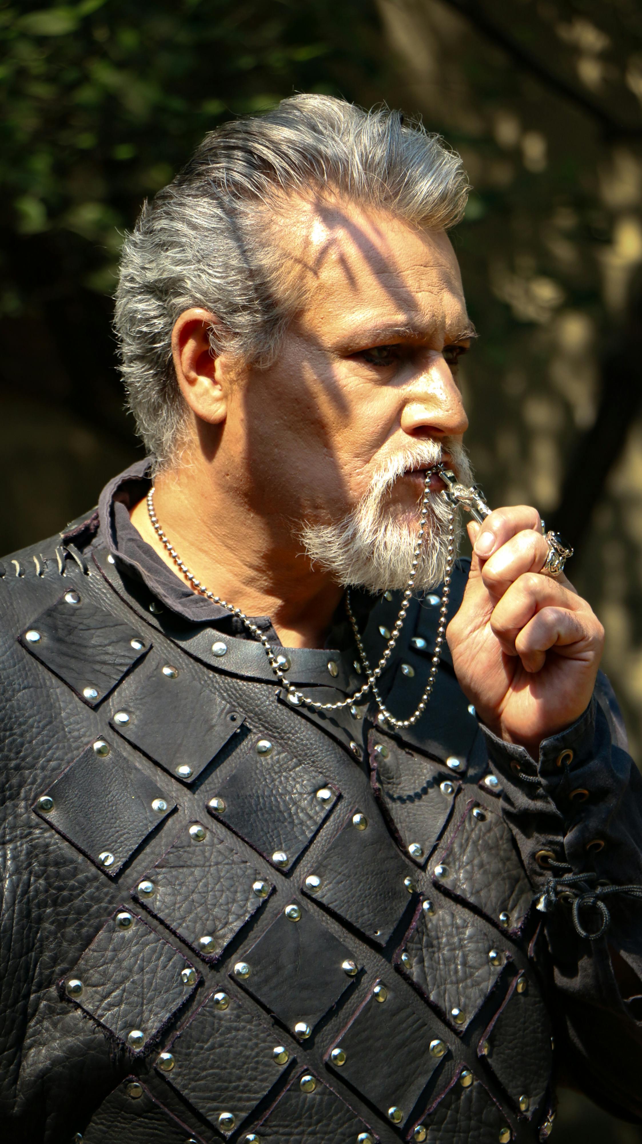 A rugged man in leather armor holding a necklace, illuminated by sunlight outdoors.