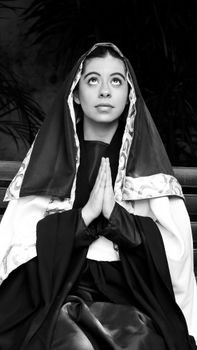 A contemplative woman in a traditional outfit praying indoors.