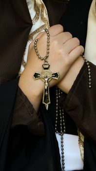 Close-up image of hands clasped around a crucifix necklace, symbolizing faith.