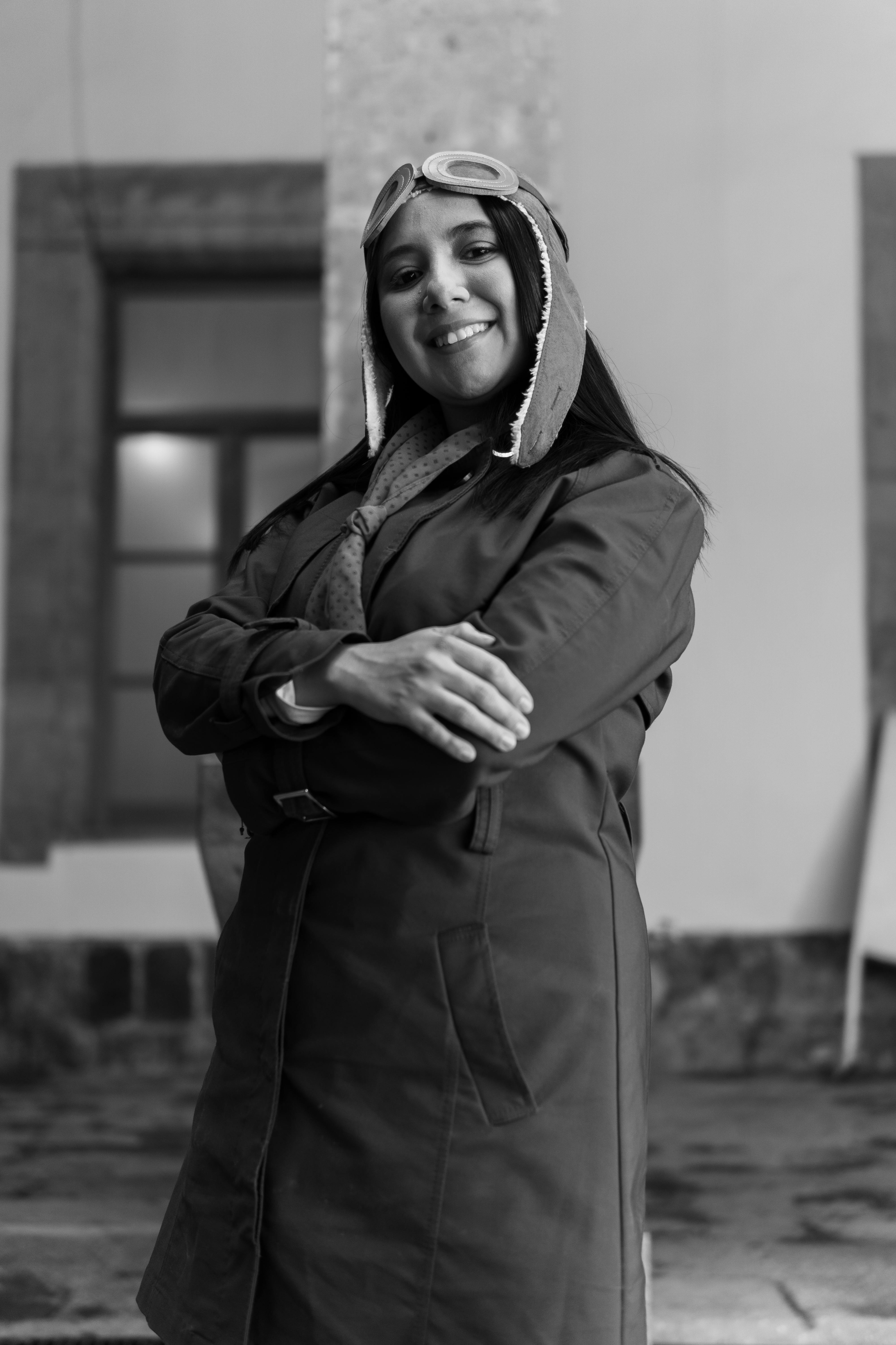 Stylish black and white portrait of a woman in an aviator hat standing confidently.