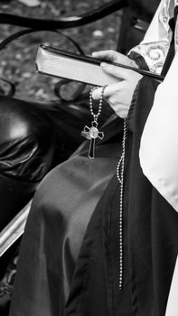 Black and white photo of a nun's hands holding a rosary and Bible, emphasizing faith and devotion.