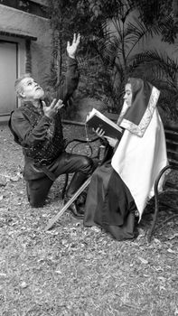 Black and white photo of a kneeling knight and seated nun in medieval attire, outdoors.