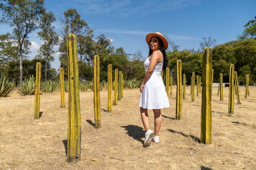 A woman in a hat and dress stands in front of tall cactus plants