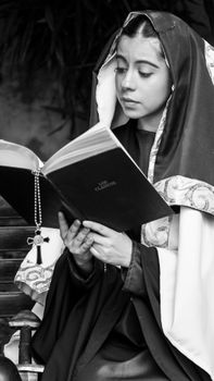 A young woman adorned in a monastic habit is deeply engrossed in reading a book, symbolizing spirituality and devotion.