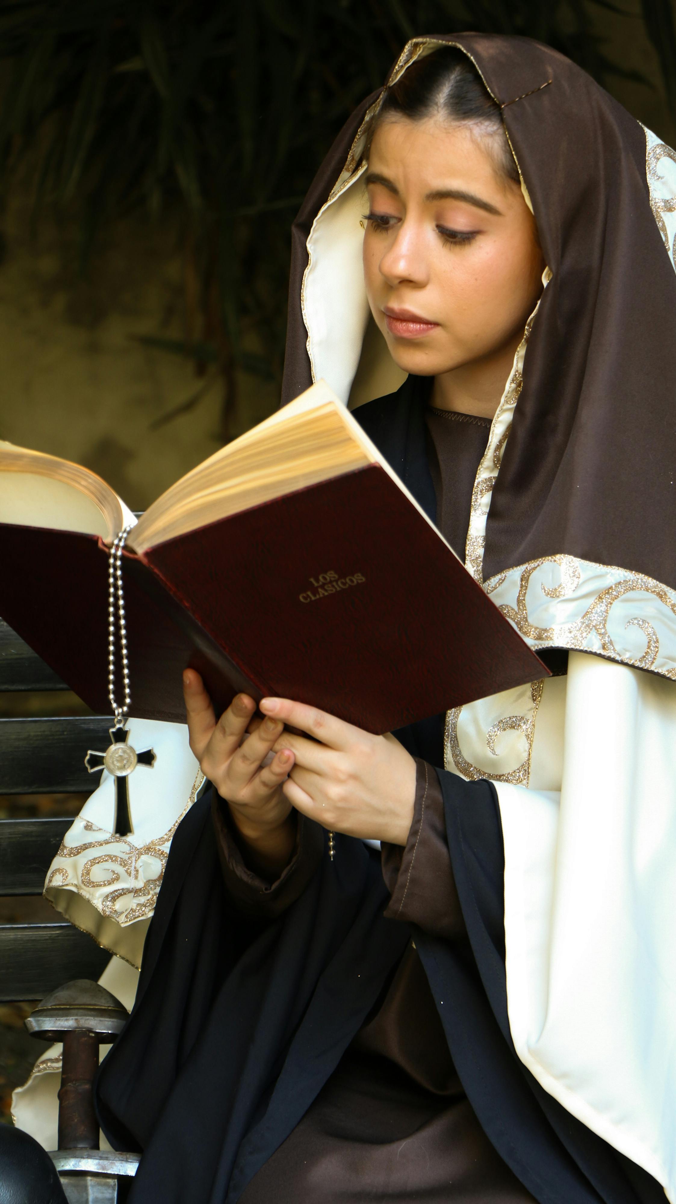 A young nun in a monastic habit reading a book with a rosary in hand, evoking spirituality and devotion.
