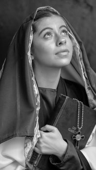 Monochrome portrait of a woman in religious attire holding a book and rosary, looking upward.