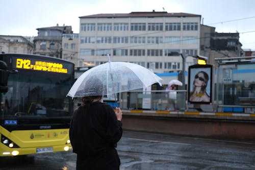 A woman holding an umbrella in front of a bus