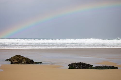 A rainbow is seen over the ocean and rocks