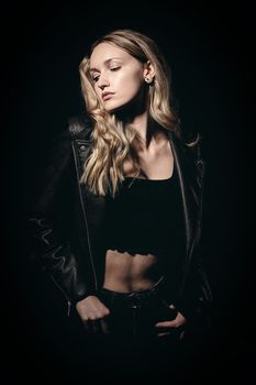 A model poses confidently in a leather jacket and crop top against a black background.