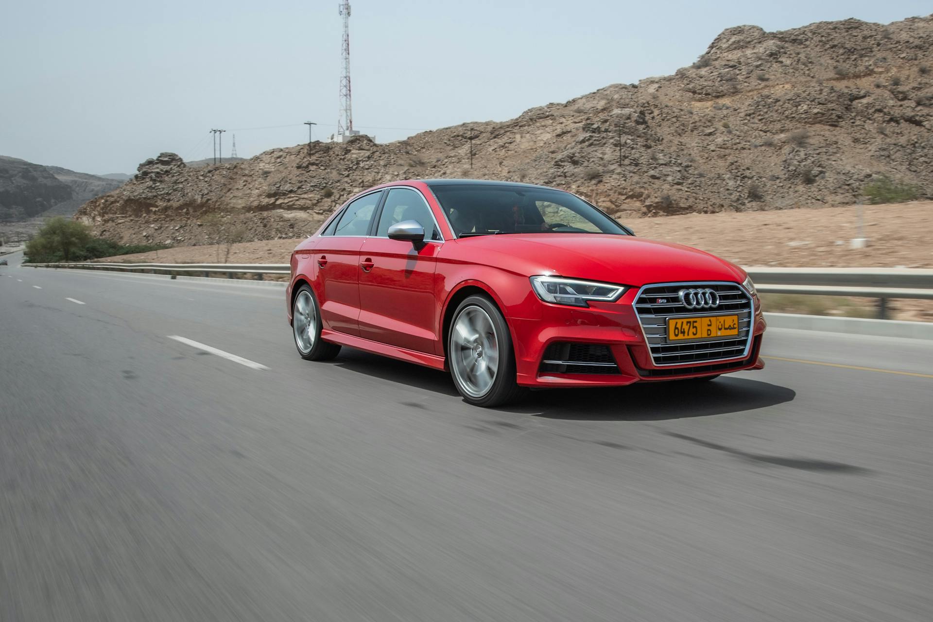 Red Audi S3 in motion on a highway near Muscat, Oman, showcasing automotive speed and elegance.