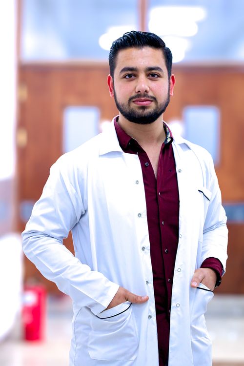 Free Confident Middle Eastern doctor in a red shirt and white gown smiling indoors. Stock Photo