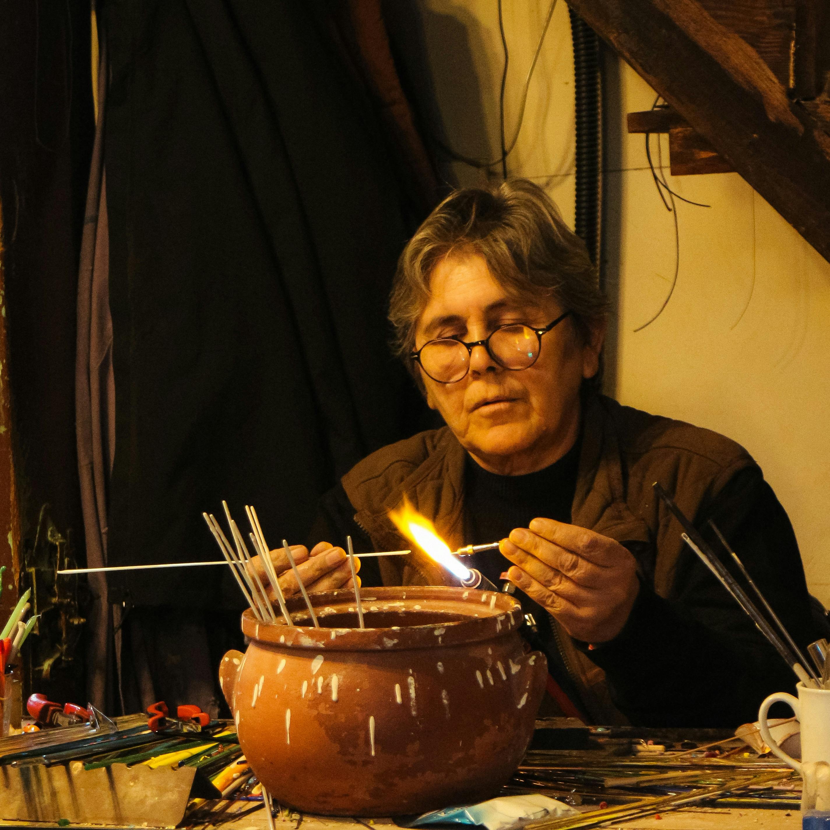 A skilled artisan carefully crafts using fire in a cozy indoor workshop setting.