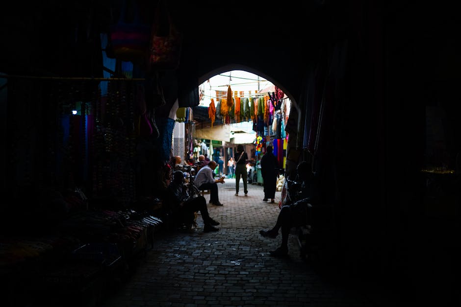 Explore a bustling Moroccan market in a dimly-lit alleyway, capturing shadows and vibrant textiles.