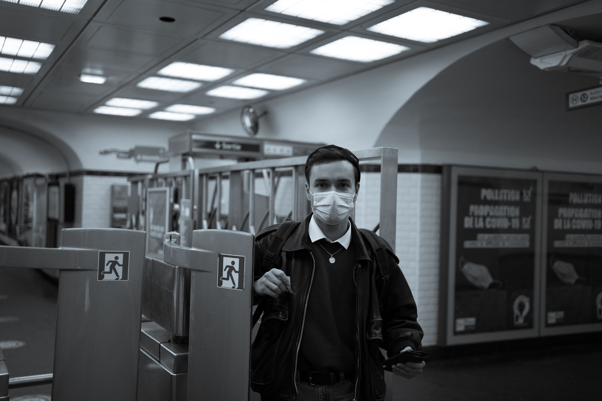 Black and white photo of a man in a face mask navigating subway turnstiles.