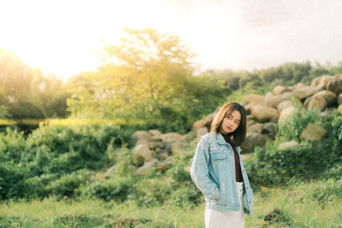 A woman in a white skirt and denim jacket standing in a field