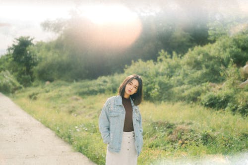 A woman in a white skirt and denim jacket standing on a dirt road