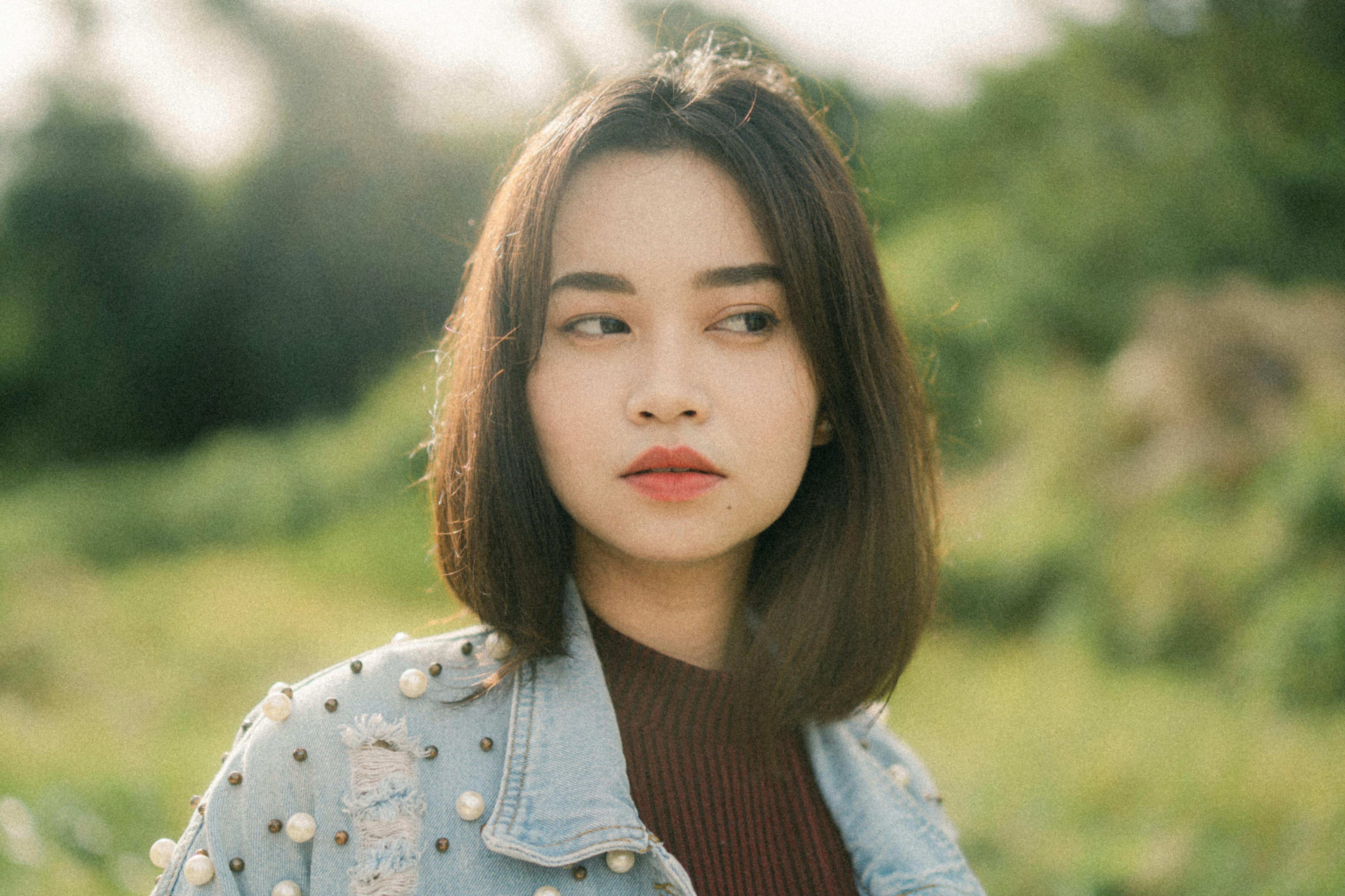 Portrait of a young woman wearing a denim jacket in a park setting.
