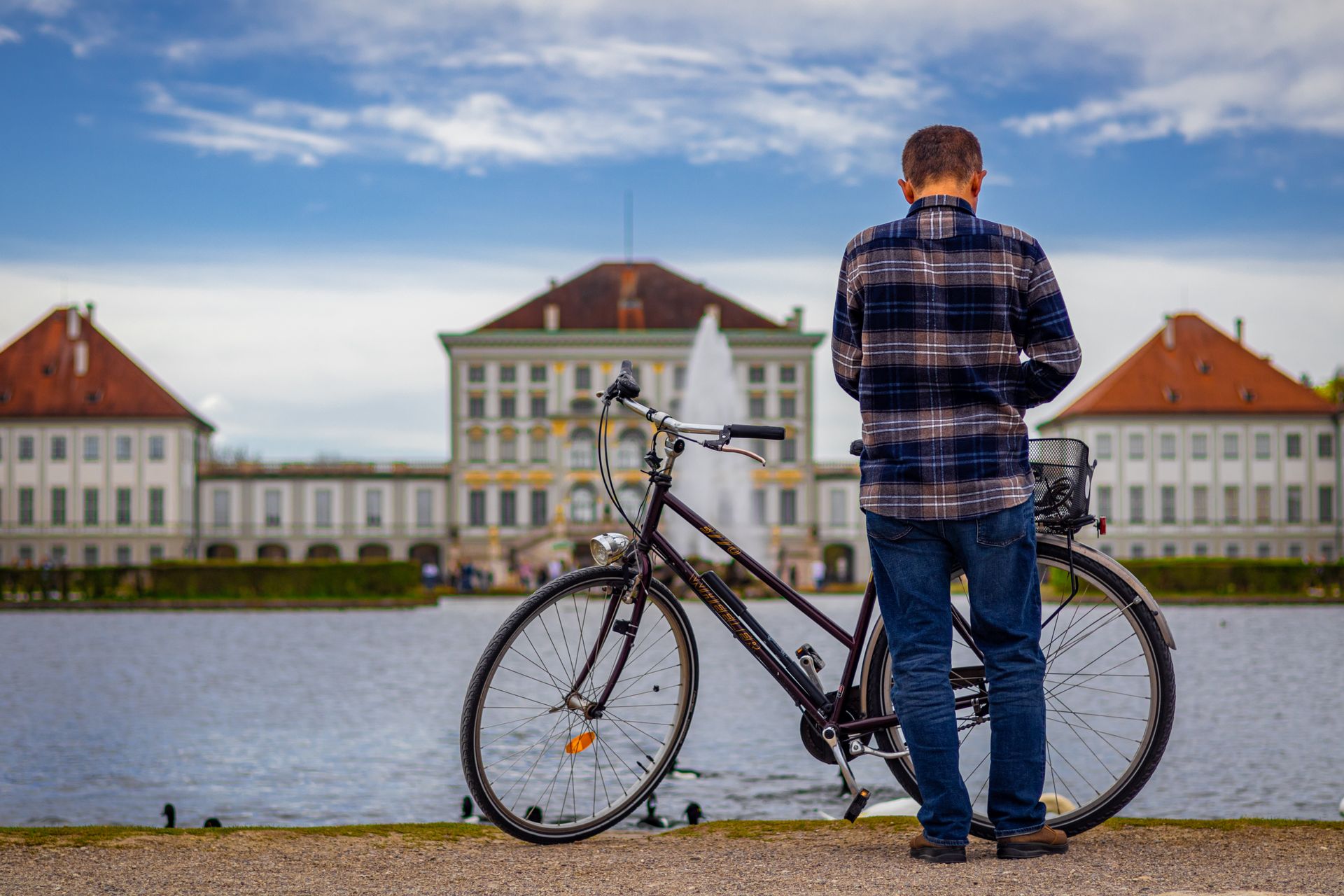 Back view of a man standing with a bicycle near Nymphenburg Palace, Munich.