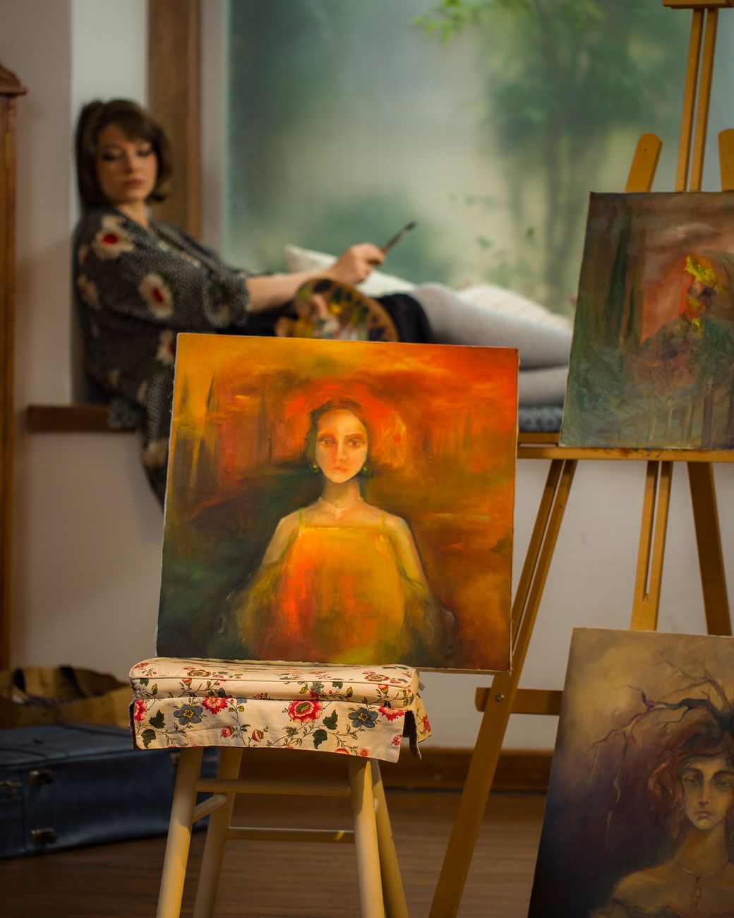 Atmospheric art studio showcasing a female painter with colorful painted canvases on easels.