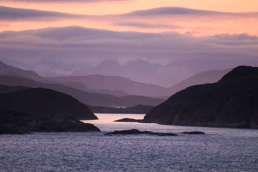 A tranquil scene capturing a misty bay at twilight, with layers of mountains and a serene ambiance.