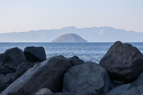 Free Explore a calm coastal landscape with rocky shoreline and distant island view under clear skies. Stock Photo
