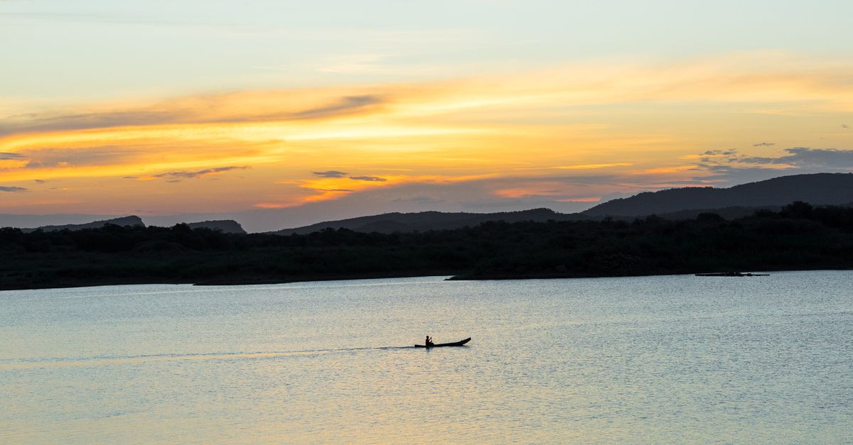 A lone kayak on the calm waters of the Volta River near Akosombo at sunset, with dense green hills in the background
