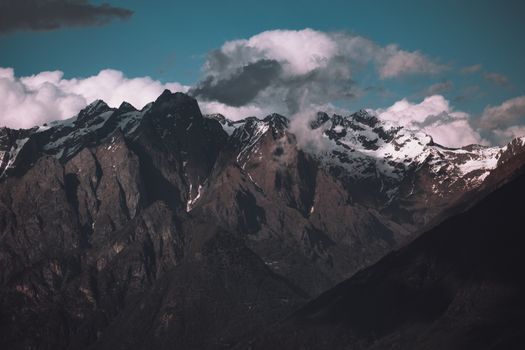 A dramatic view of snow-capped mountain peaks enveloped by clouds, showcasing the rugged beauty of nature.
