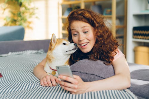 A woman is smiling while holding a dog and looking at a phone