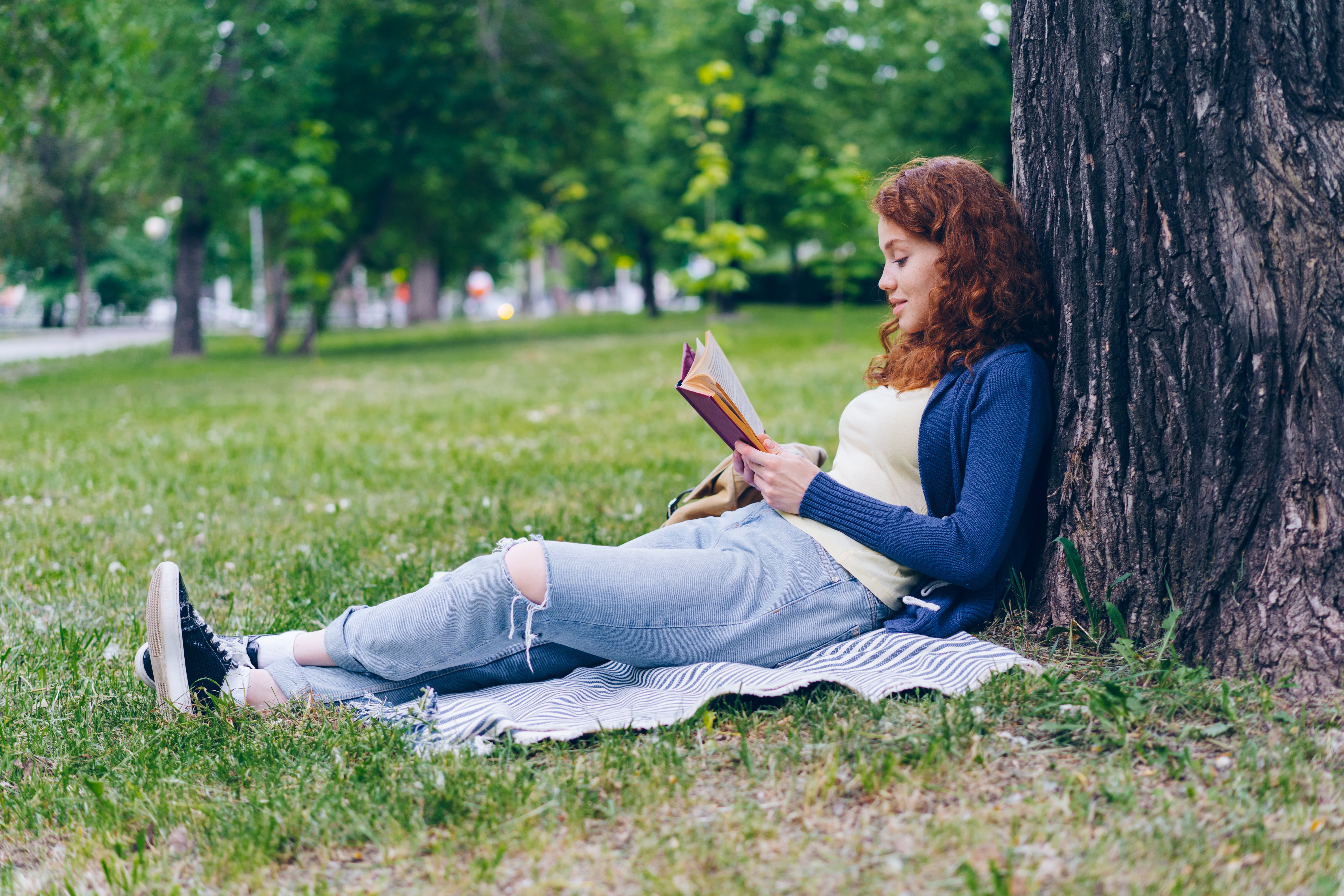A young woman enjoys reading a book while relaxing in the park during a sunny summer day.