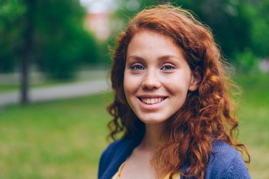 Portrait of a cheerful young woman with red hair in a green outdoor setting.
