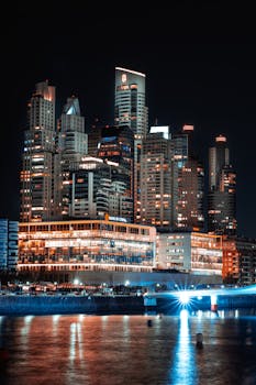 Illuminated Buenos Aires cityscape with modern skyscrapers reflecting on the river at night.