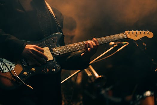 Musician playing electric guitar on stage with dramatic lighting.