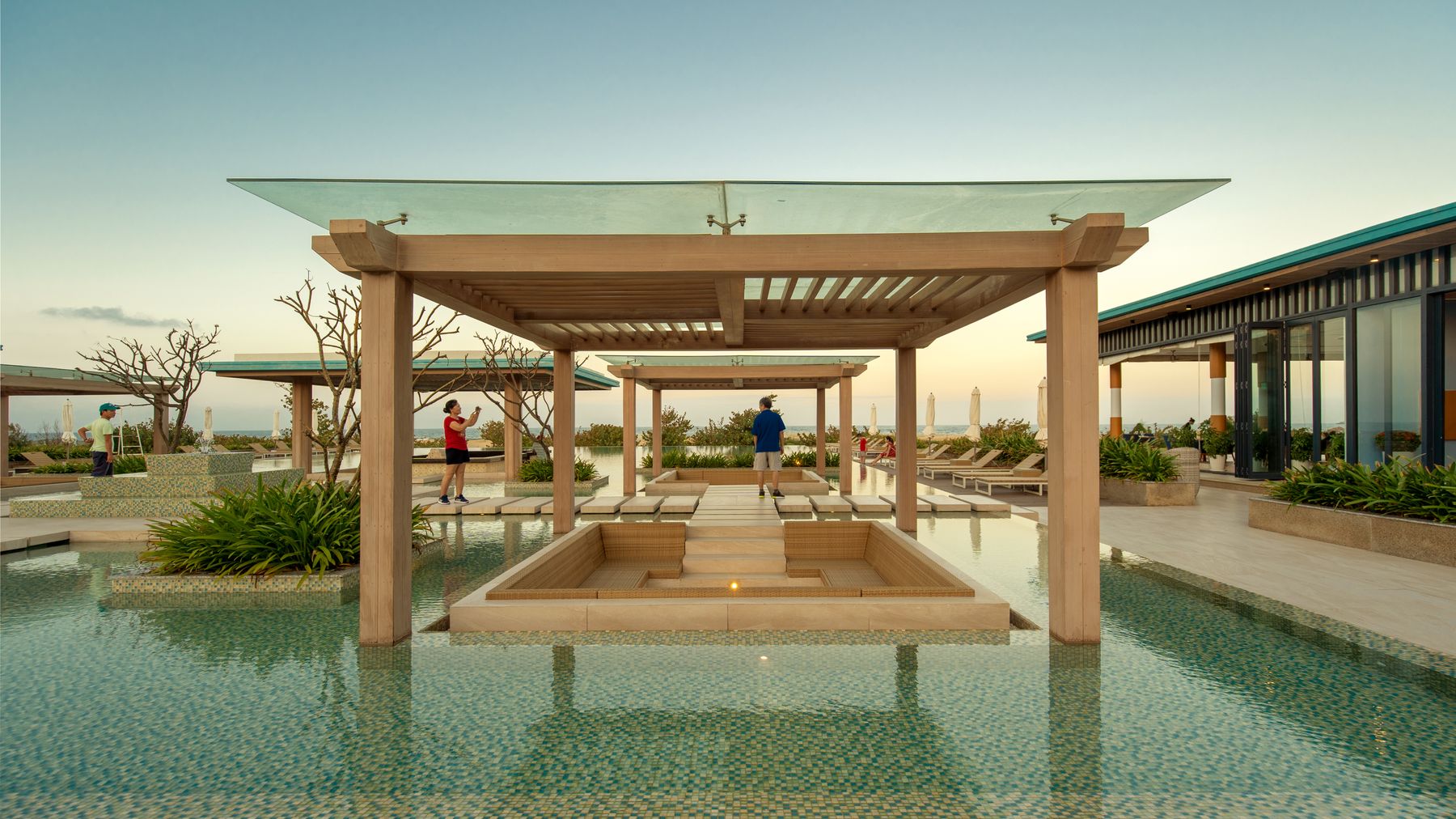 Elegant resort pool area with tourists and modern design at sunset in Vietnam.