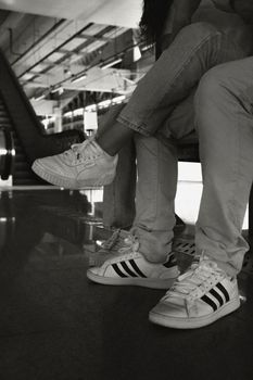 Two people sitting indoors, showcasing casual style with sneakers and jeans.