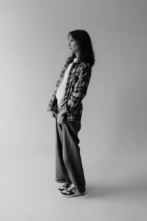 Free A woman in plaid shirt and jeans standing in front of a wall Stock Photo