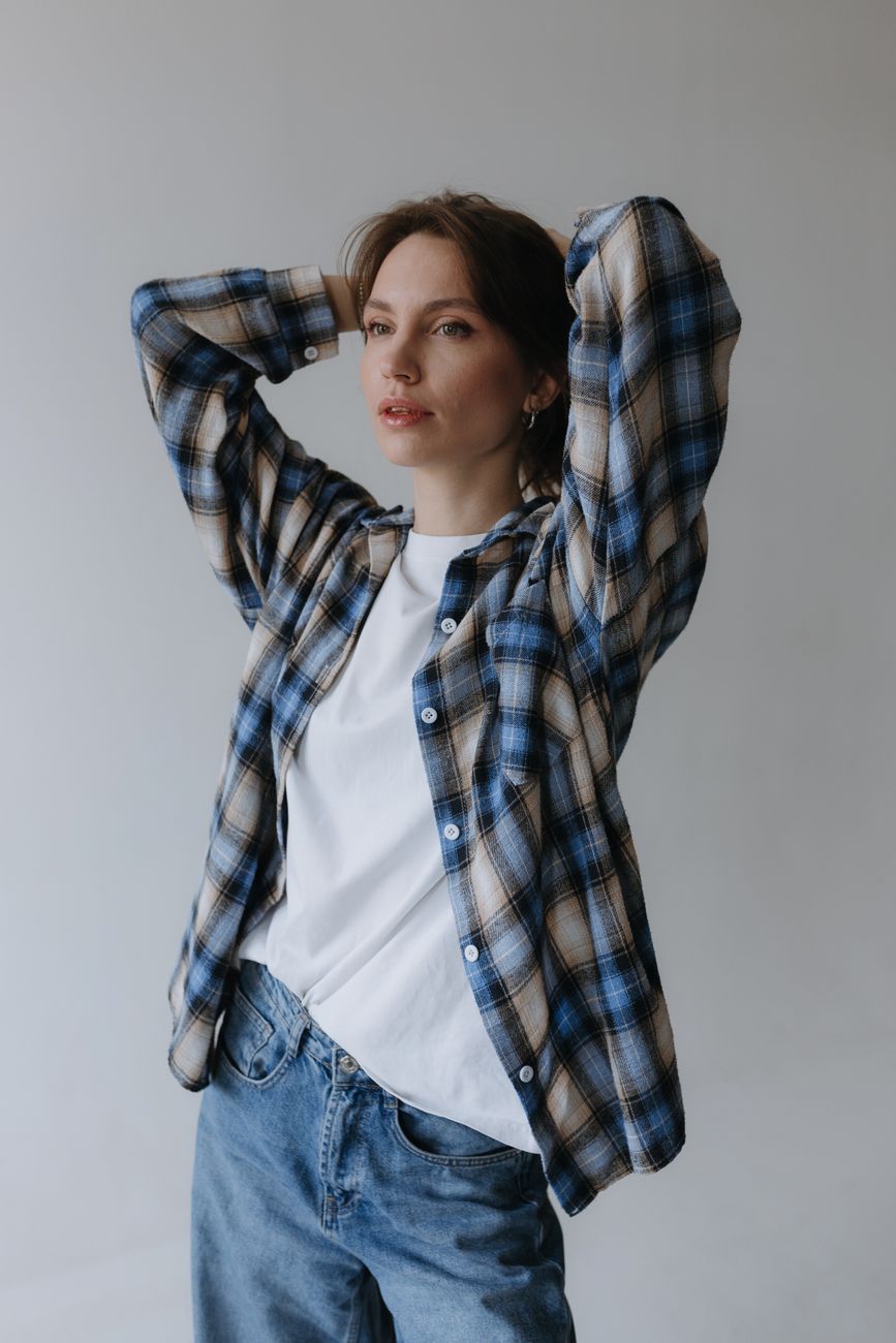 Woman in casual plaid and jeans posing confidently in studio setting.
