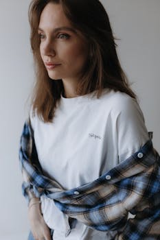 Stylish young woman wearing a plaid shirt over a white t-shirt, posing in a modern indoor setting.