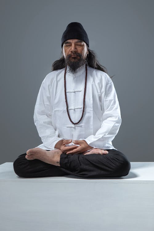 A man in a white shirt and black pants sitting in meditation