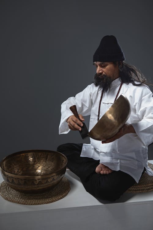 A man with long hair and beard is playing a tibetan singing bowl