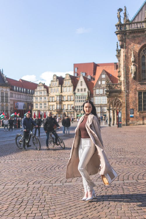 A woman in a long coat and white pants is walking down a street