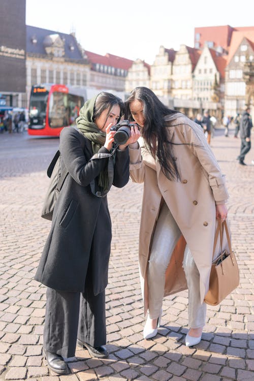 Two women taking pictures of each other in a city