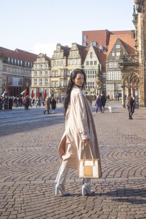 A woman in a long coat and white shoes is walking through a city